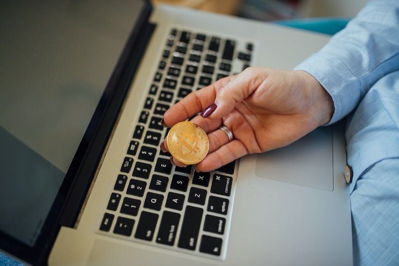 Een hand met een bitcoinmunt boven het toetsenbord van een laptop